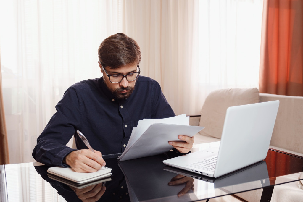 Entrepreneur in eyeglasses works with a laptop and keeps a document in a home office