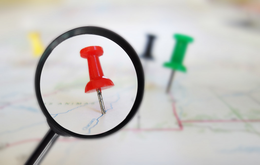 A magnifying glass viewing pins on a map